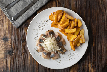 Appetizer for beer. Pieces of salted herring with onions and fried potato slices in a plate on a wooden table. Horizontal orientation, no people, top view