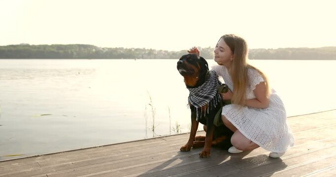 Young woman stroking black rottweiler on lake pier
