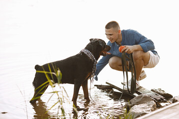 Man with rotweiller dog playing together in the lake