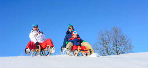 Junge Familie bei der gemeinsamen Rodelpartie im Schnee