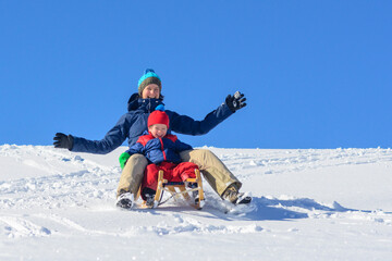 Mutter und Kind haben Spass beim Rodeln an einem sonnigen Wintertag