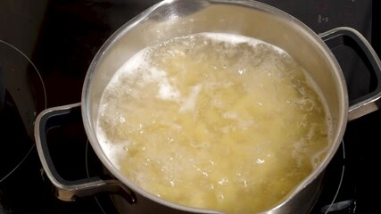 Hand stirring raw pasta boiling in boiling water in a metal pot on the stove, close-up, full hd. The cooking process of a traditional dietary vegetarian meal. Homemade food concept - Powered by Adobe