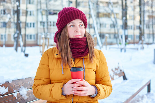young woman in a benny hat and a yellow jacket with a disposable cup of coffee in her hands on a frosty winter day