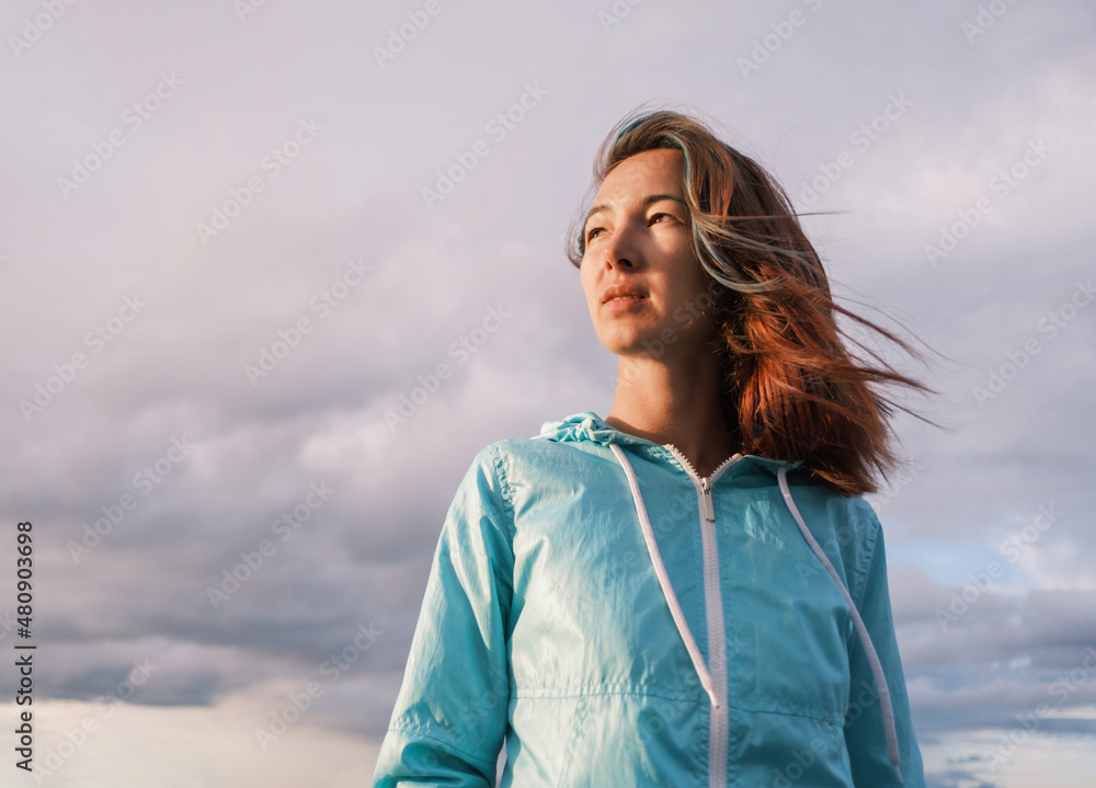 Wall mural portrait of a young woman with fluttering hair during the sunset. cloudy sky in the background.