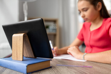 school, education and distant learning concept - close up of tablet pc computer and teenage student girl writing to notebook at home