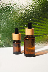 Amber glass bottles with dropper pipette with serum or essential oil against the background of corrugated glass. Skincare cosmetic with palm leaves shadows. Beauty concept for face body care