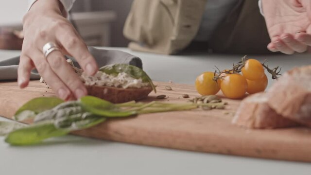 Slowmo close up of unrecognizable hands adding pumpkin seeds on blue cheese tomato bruschetta on wooden plate