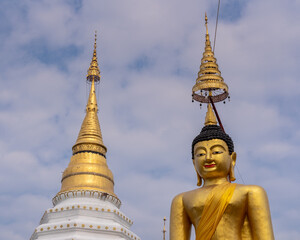 Fototapeta premium Low angle view of golden buddha statue and ancient stupa on blue sky with clouds background at historic Wat Chiang Yuen buddhist temple, Chiang Mai, Thailand