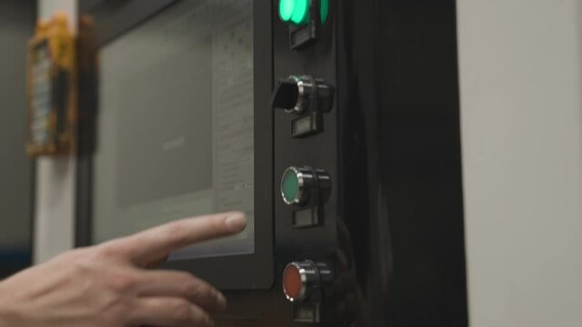 Close up of hand pressing green button of industrial CNC machine, start program