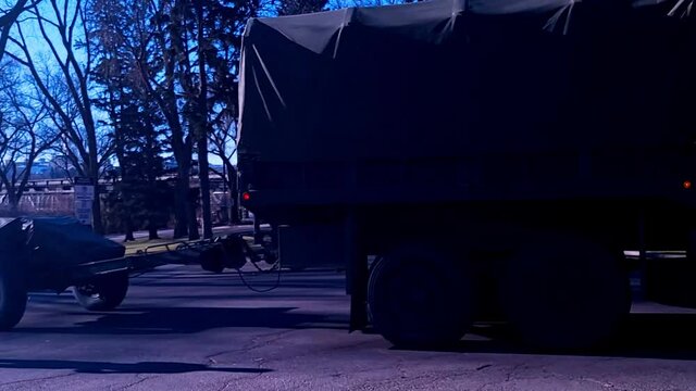 Military Truck DEW with 6 wheels hauling 2 wheeled mobile canon called C3 Howitzer with covering from parking lot on a sunny brisk fall day from a Remembrance Day ceremony by Canadian military person