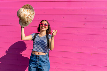 young woman with a horizontal striped T-shirt caught by the wind catches her hair on the fly, pink background, generation z - obrazy, fototapety, plakaty