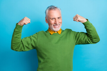 Photo of pretty strong retired man wear green sweater rising fists isolated blue color background