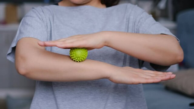 Close-up a young woman in a short topic is working out the arm muscles with a green myofascial ball. Woman doing exercises with rubber ball, closeup.