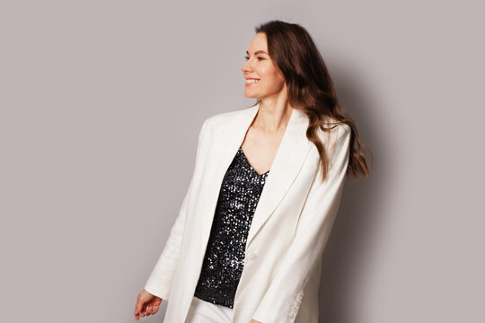 Young pretty brunette woman in white jacket and sequins t-shirt, smiling