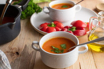 Paprika soup with tomatoes, onions and  garlic served in white cups on wooden table