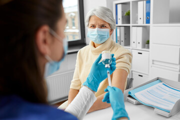 medicine, health and vaccination concept - doctor or nurse filling syringe with vaccine or drug and senior woman at hospital