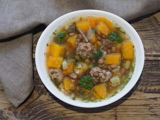Pumpkin soup with meatballs and lentils in a white bowl, napkins autumn leaves on a wooden background, top view. Recipe for seasonal healthy soup 
