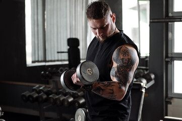 Muscular tattooed athlete doing exercises with dumbbells in the gym