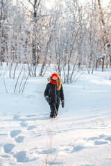 Fototapeta na wymiar Cute little girl 10 years old in a red hat in a winter forest with sunlight. A little girl is having fun on a winter day. cheerful little girl in a warm jumpsuit