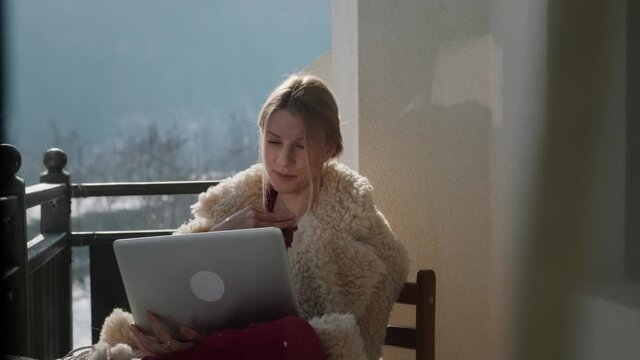 Young woman with laptop freelancing at winter chalet on the balcony.