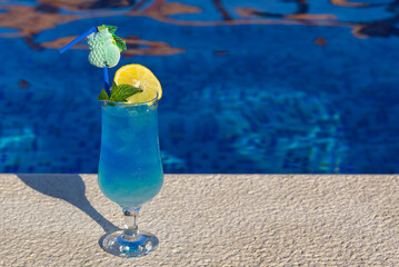 Blue Lagoon Beach Cocktail with fresh lemon standing by the swimming pool. Summer tropical cocktail.