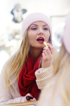  blond girl in red scarf make up her lips with red lipstick close up photo on Christmas shopping mall background