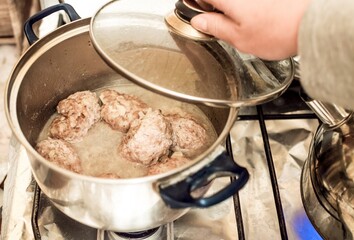 Hand removes lid, steel pan with stewed meat patties