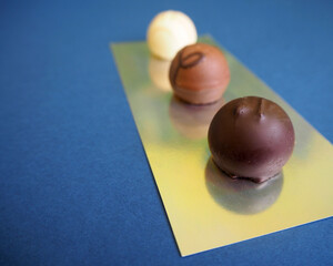 three round candies made of white, milk and dark chocolate stand with a shiny surface on a blue background. side view. sweets. round candies