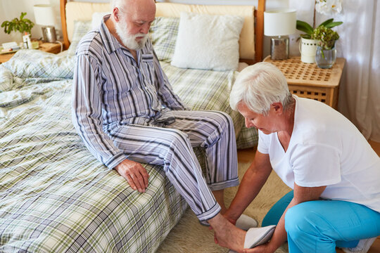 Pflegekraft vom Pflegedienst hilft Hausschuhe anziehen