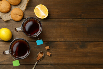 Tea bags in glass cups of hot water, cookies and sugar cubes on wooden table, flat lay. Space for text