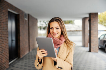 Fototapeta na wymiar A businesswoman with a tablet outdoors. A happy businesswoman in warm clothes standing outdoors and using the tablet for web research.