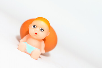 Miniature newborn baby toy and egg sitting on a white gray background.Selective focus,copy space.