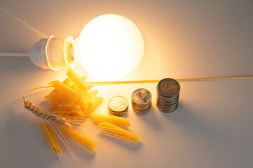 Ear of wheat, pasta, light bulb and coins, on white surface. Price of energy and wheat, which...