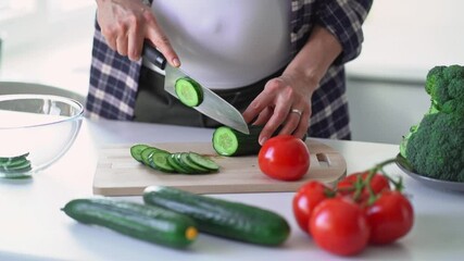 Unrecognisable pregnant middle age woman chopping fresh vegetables in modern light kitchen. Healthy eating, vegetarian, eco food