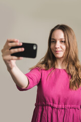 Naklejka premium Young millennial woman in pink dress with long hair makes a selfie at home.