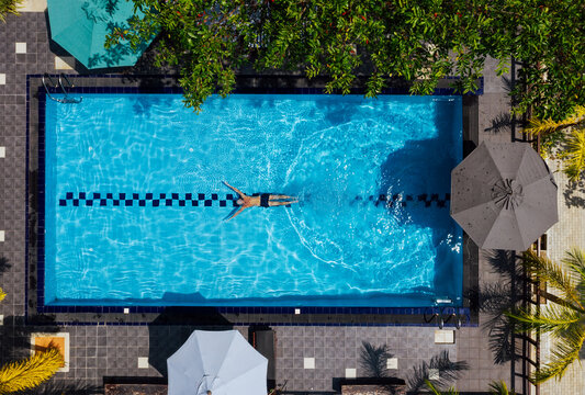Underwater swimmer man diving in the luxury villa swimming pool. Aerial top shot. Careless summer vacation concept image.