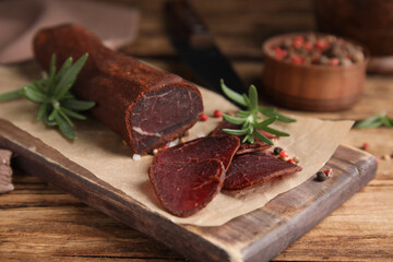 Delicious dry-cured beef basturma with rosemary and peppercorns on wooden table, closeup