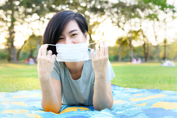 Beautiful healthy, happy Asian woman smile, take off medical face mask to cover mouth, lie down on...