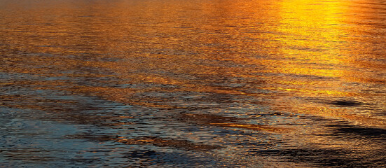 Gold water background during sunset or sunrise with waves and sunny reflection.