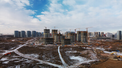 Construction site. Construction of modern high-rise buildings. Work construction cranes. Snow covered earth. Aerial photography.