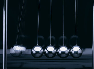 Newton-Pendel mit 5 silber-farbenen Kugeln in einer Reihe, seitlich fotografiert vor schwarzem Hintergrund