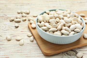 Bowl with uncooked white beans on wooden table