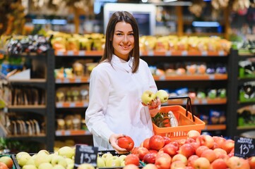 woman in a supermarket at the vegetable shelf shopping for groceries, she is choosing