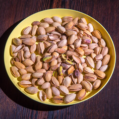 Pistachio nuts in a yellow bowl on a wooden background, side view, copy space