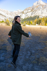Full body portrait of happy woman smilling at the camera in movement. Nature mountains background. Natural lighting and shade. Warm autumn clothes.