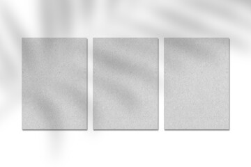 Fototapeta premium Three blank grey kraft paper cards, vertical A4 poster or business card mockup on a white background with leaf shadow. Flat lay, top view. For advertising, brand design, stationery presentation.