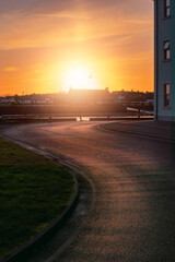 Small S shaped road in town reflects warm sun light at sunset. Vertical image. Urban scene with building silhouette in the background. Dramatic sky. Warm and cool tone.