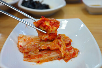 Chopsticks holding kimchi on a white plate.
