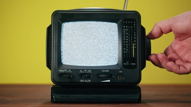 Small old television with grey interference screen on yellow background. Close-up of vintage tv on table, nostalgia. Gray noise screen and glitches, searching channel.