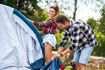 Fototapeta premium Young nice couple having fun on camping setting up tent